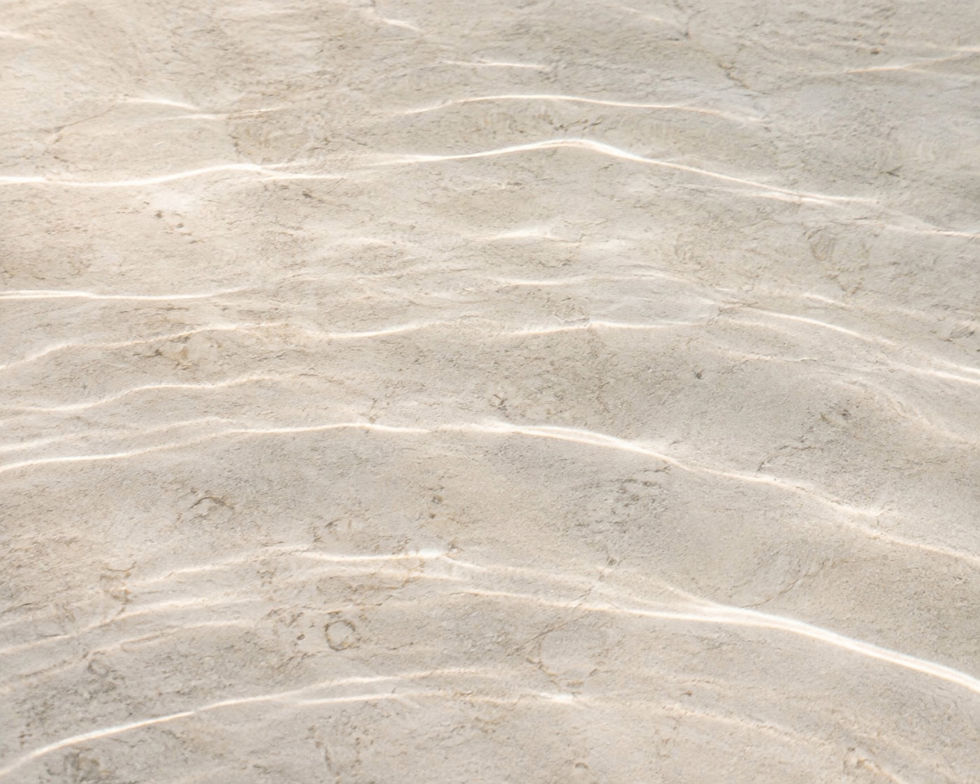 Soft ripples of light across pale stone beneath clear, shallow water.